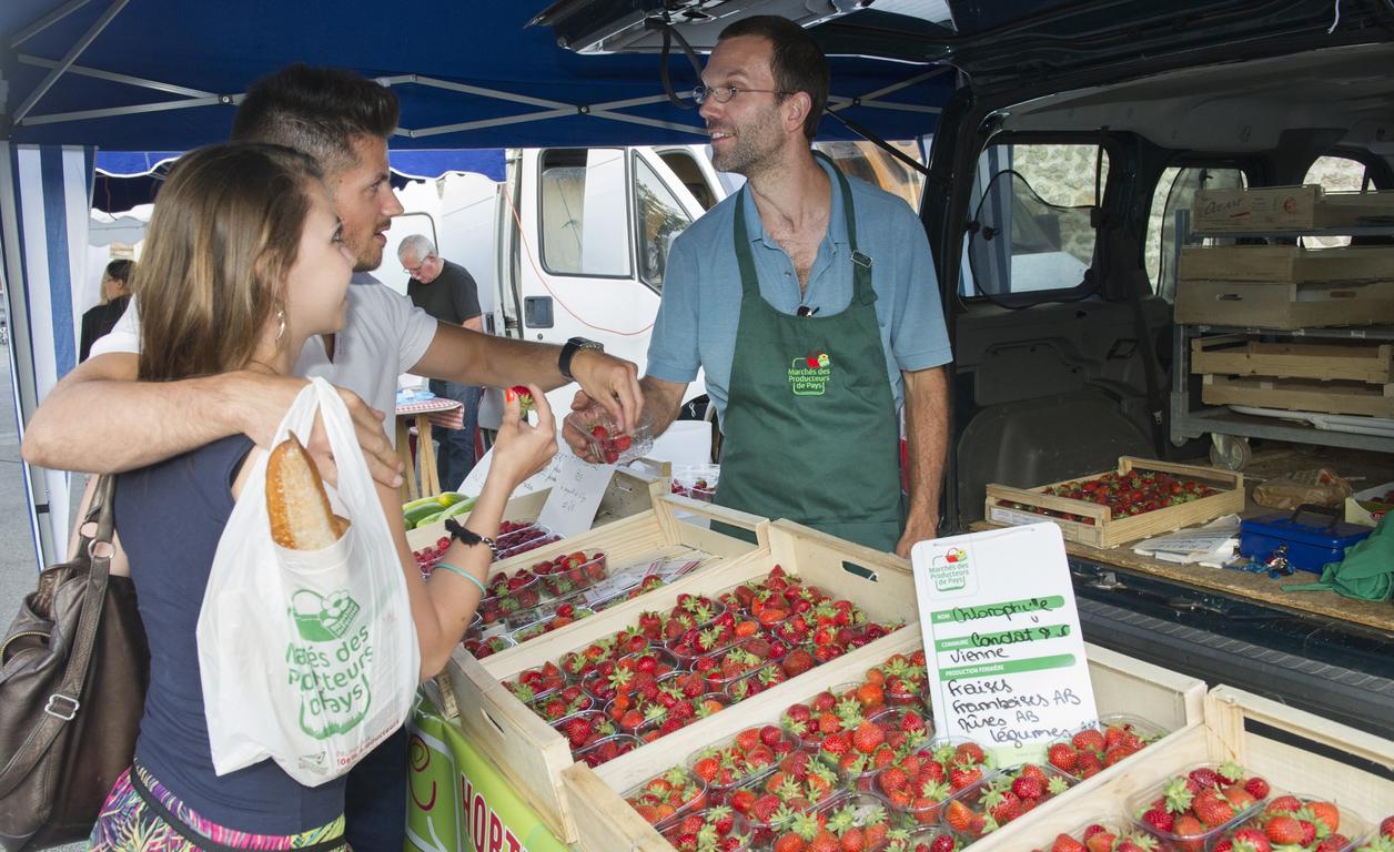 Un agriculteur fait goûter ses fraises à un couple, sur le stand au marché.