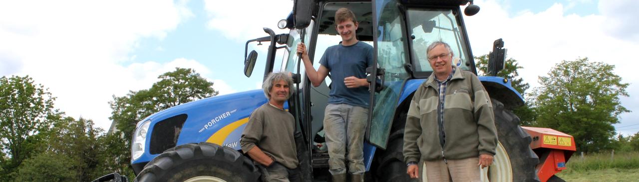 Un jeune apprenti agricole encadré par ses deux maîtres d'apprentissage devant un tracteur au milieu d'un champ.